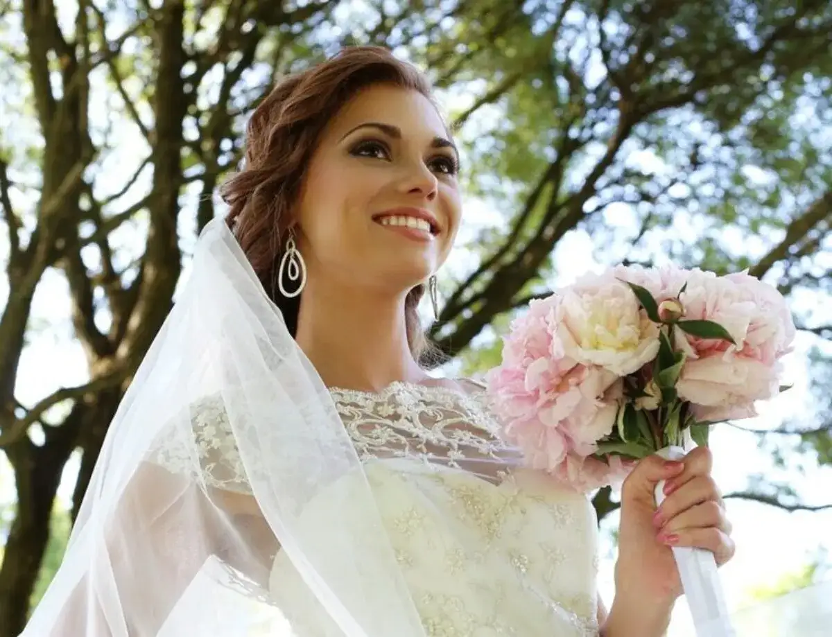 Novia sonriente con velo y ramo de peonías rosas, lista para su boda gitana.
