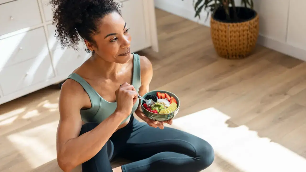 Donna con capelli ricci mangia una ciotola di frutta colorata, un pasto sano che aiuta a dimagrire.