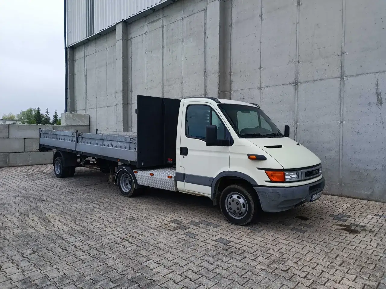 Biały Iveco z przyczepą, gotowy do transportu. Ten ciągnik jednoosiowy z przyczepą to niezawodny pomocnik w pracy.