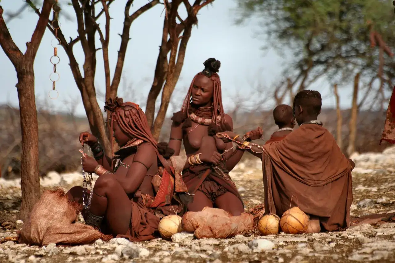 Afrykańskie plemiona Himba w tradycyjnych strojach i biżuterii, siedzące pod drzewem.