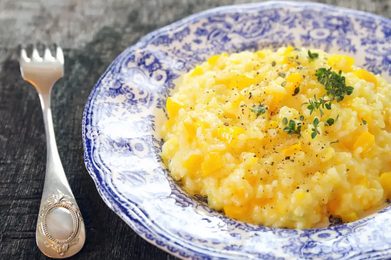 Pyszny, kremowy **ryż do risotto** z kawałkami dyni, udekorowany świeżym tymiankiem i pieprzem. Obok leży srebrny widelec.