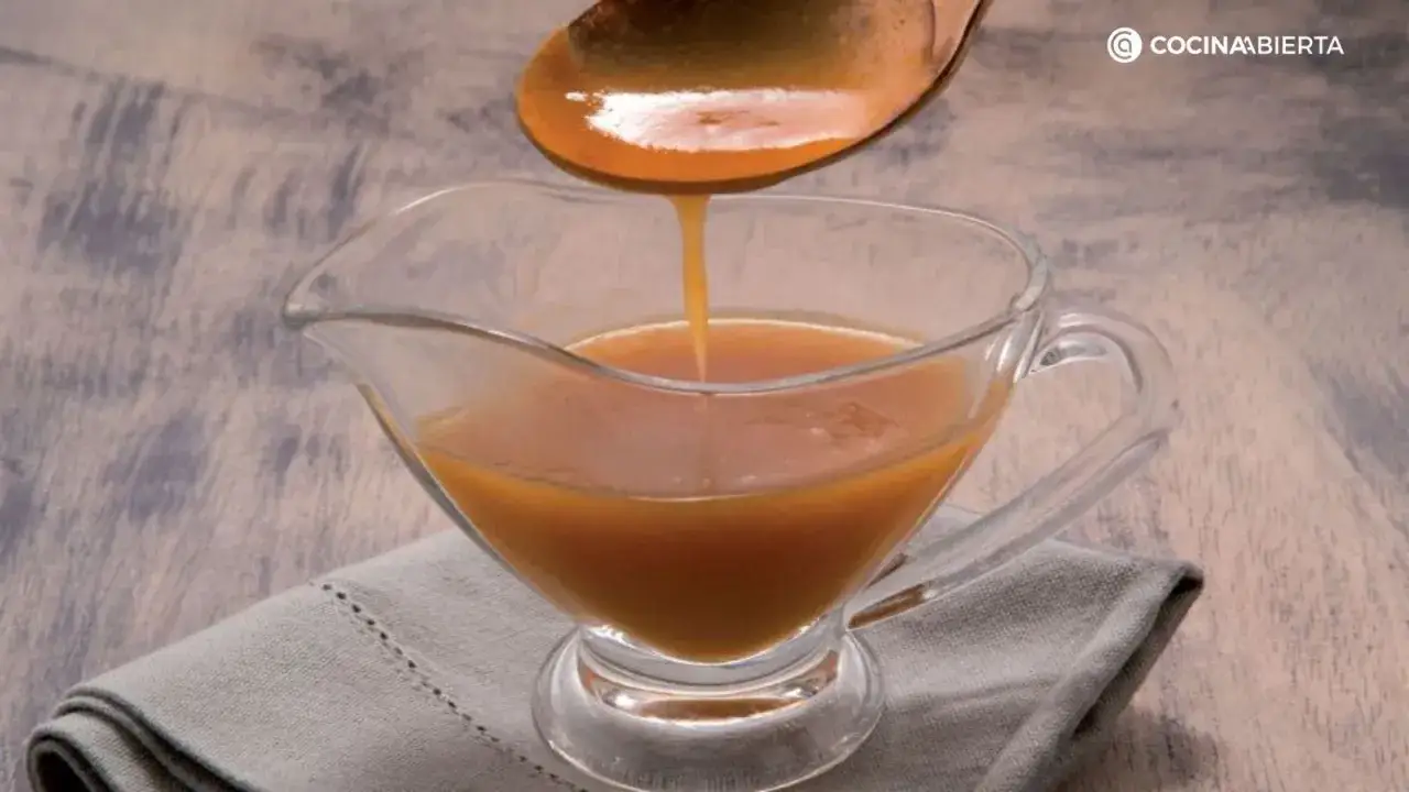 Cuchara vierte salsa dorada en una salsera de cristal. La maicena ayuda a espesar salsa para un acabado perfecto.
