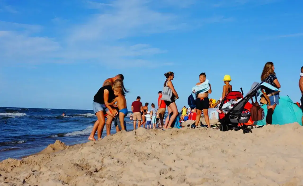 Rodziny cieszą się słońcem i piaskiem na kąpieliskach nad Bałtykiem. Dzieci bawią się na plaży, a dorośli odpoczywają.