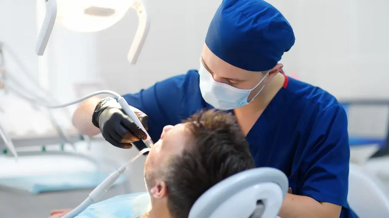 Dentysta w masce i rękawiczkach wykonuje zabieg. Sen o dentystach może oznaczać troskę o zdrowie lub potrzebę zmian.