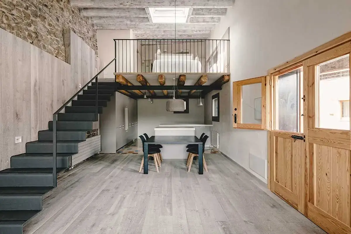 Interno moderno con scala a vista e soppalco aperto. Tavolo da pranzo e cucina a vista sotto il soppalco.