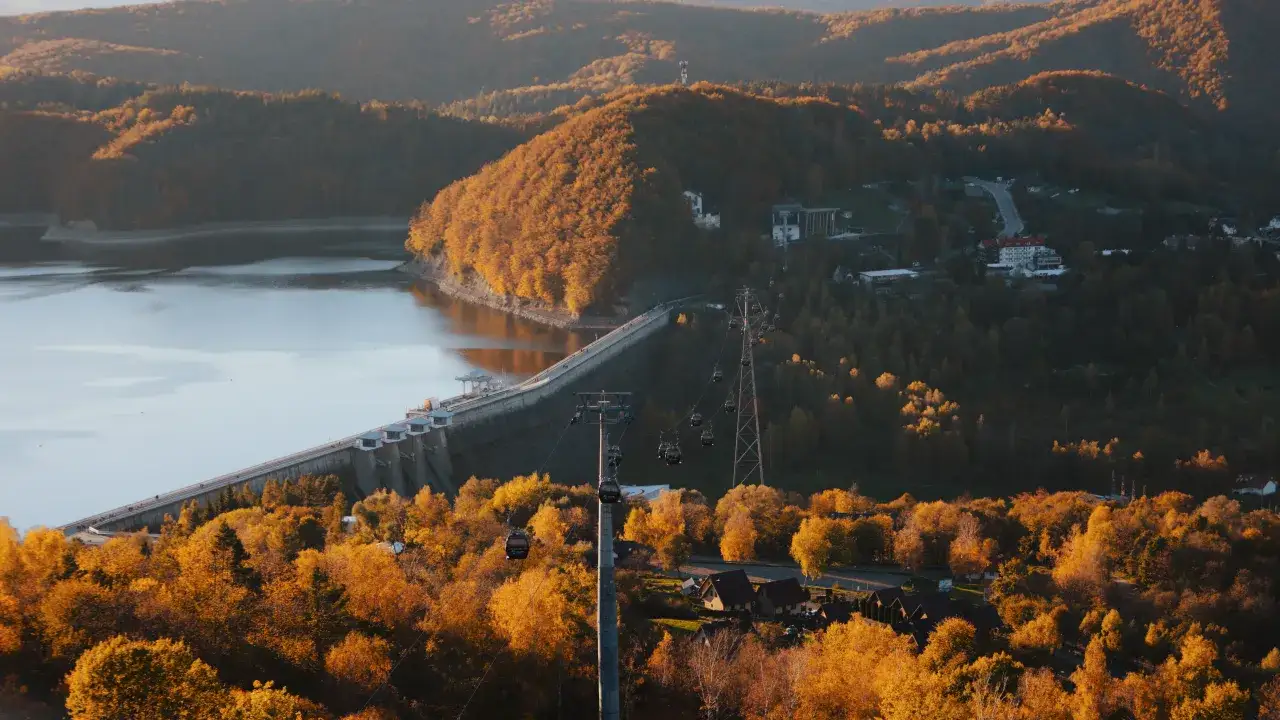 Olchowiec nad Soliną w jesiennej szacie. Kolejka gondolowa sunie nad złotymi drzewami, ukazując majestatyczną zaporę.