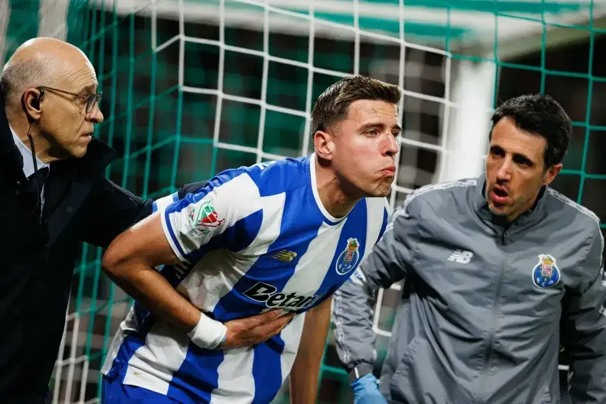 Piłkarz w niebiesko-białej koszulce FC Porto, Jan Bednarek, trzyma się za brzuch, wyraźnie odczuwając ból. Dwóch członków sztabu medycznego pomaga mu zejść z boiska.