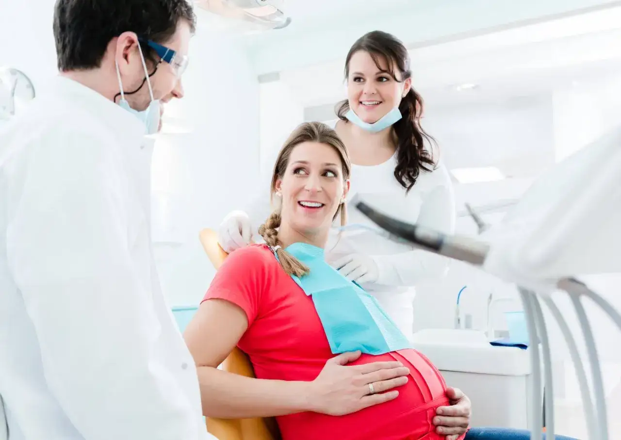 Uśmiechnięta ciężarna pacjentka u dentysty, która nie odczuwa bólu zęba w ciąży dzięki troskliwej opiece.
