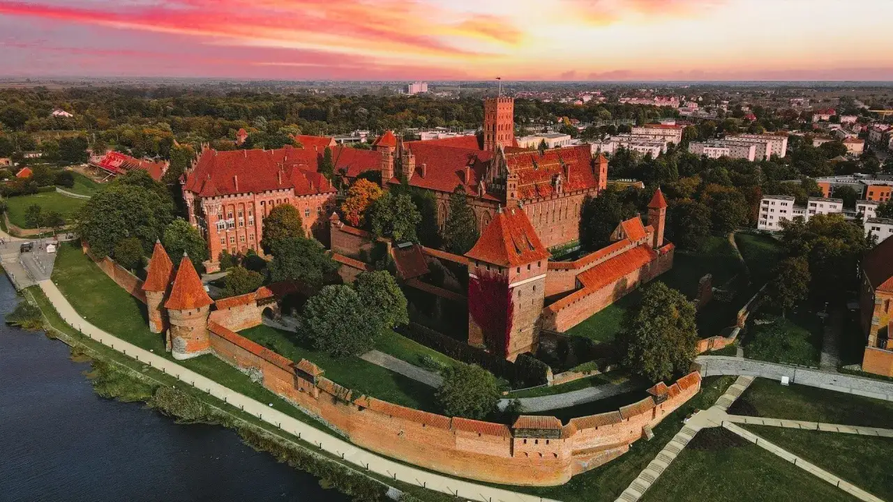 Zamek w Malborku o zachodzie słońca, z czerwonym niebem. Imponujące mury i wieże tej twierdzy to jedne z najpiękniejszych atrakcji Polski.