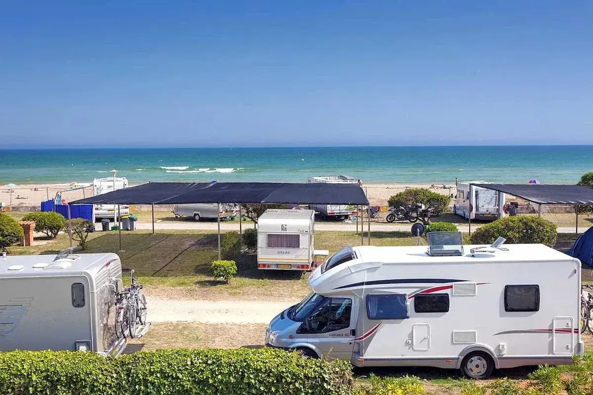 Autocaravanas y caravanas en un camping junto al mar, ideal para camping en Barcelona. El mar azul y la playa invitan a disfrutar del sol.