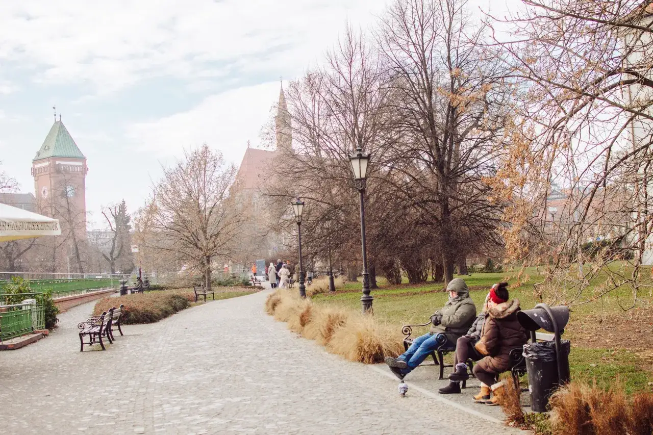 Wrocławskie bulwary to idealne miejsce, gdzie na spacer we Wrocławiu. Dwie osoby odpoczywają na ławce, w tle wieża ciśnień i kościół.