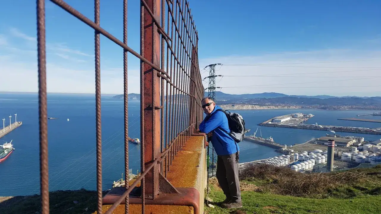 Hombre con mochila en Punta Lucero, disfrutando de la vista del puerto y el mar azul.