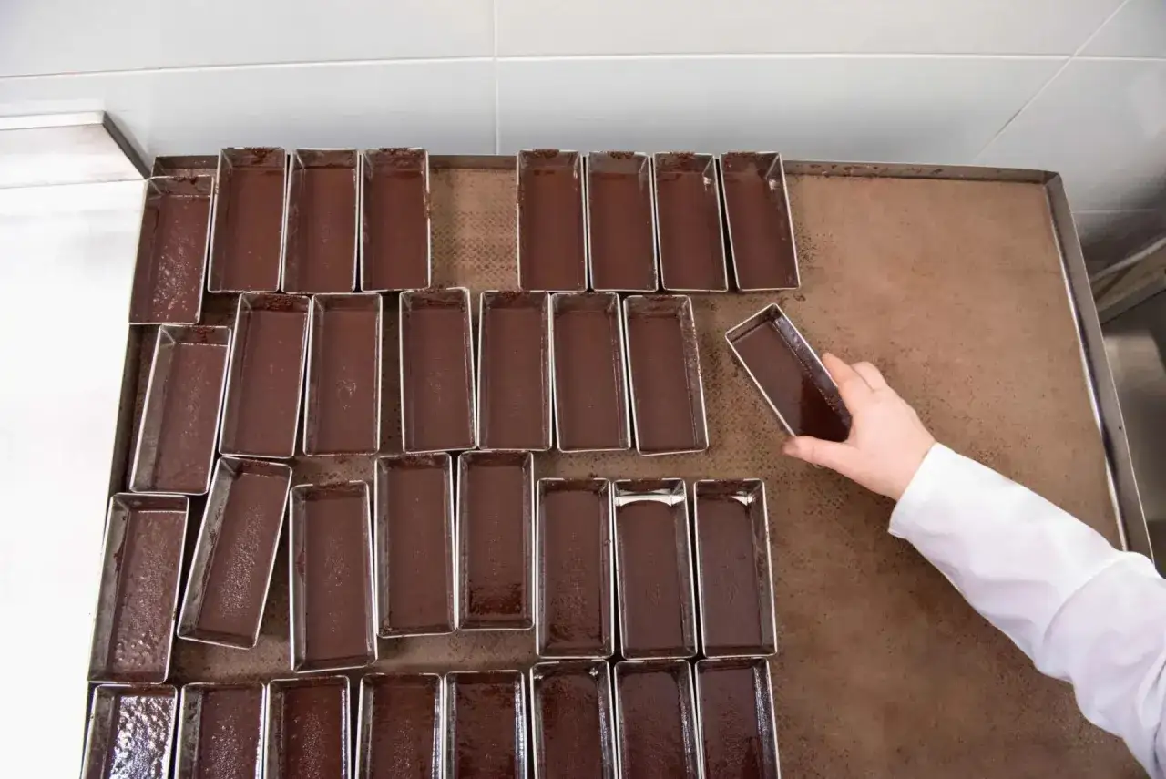 Mani esperte posizionano stampi pieni di cioccolato lavorato a freddo, pronti per diventare delizie.