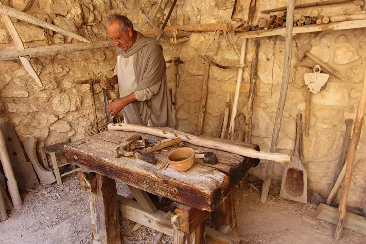 A man in ancient garb works wood, a scene that might have been familiar to Jesus, the carpenter, as he crafted his trade.
