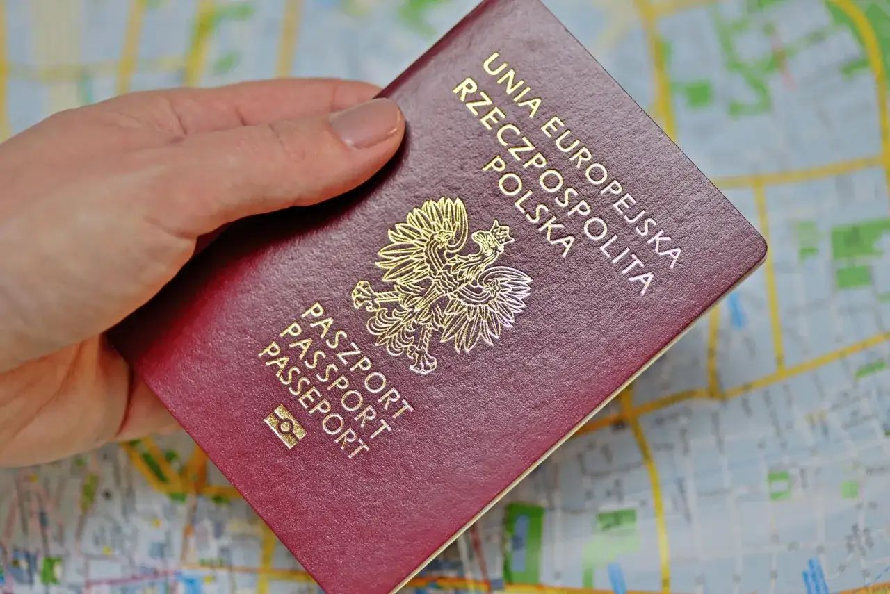 Dłoń trzyma polski paszport na tle mapy. Chip w paszporcie polskim jest niewidoczny na okładce.