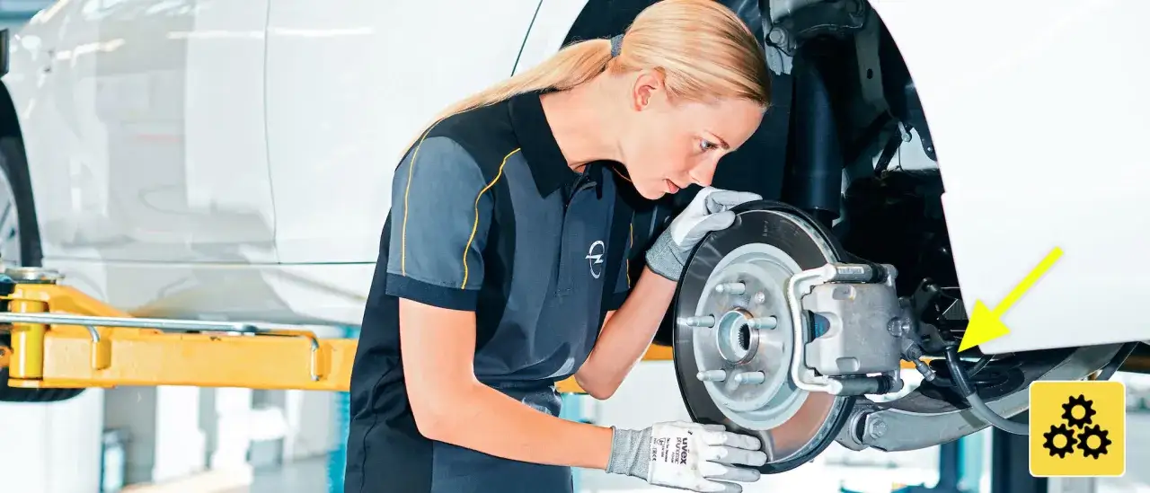 Mechanik w rękawiczkach sprawdza hamulec ręczny. Wymiana linki hamulca ręcznego jest kluczowa dla bezpieczeństwa.