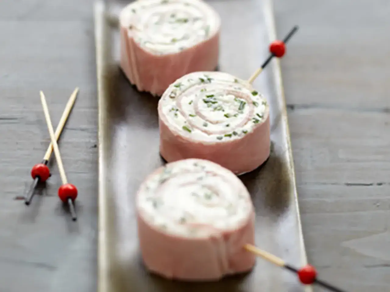 Trois rouleaux de wrap jambon garnis de fromage frais et ciboulette, servis sur un plateau.