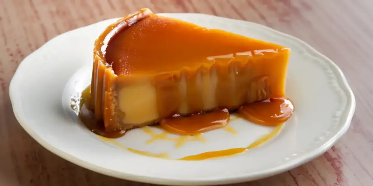 Rebanada de flan de leche condensada con caramelo l&iacute;quido cayendo sobre un plato blanco.