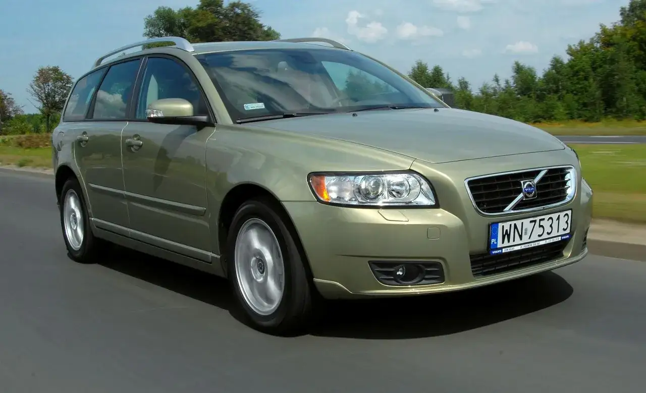 Złoty Volvo V50 1.6 diesel w ruchu drogowym, z zielonymi drzewami w tle.