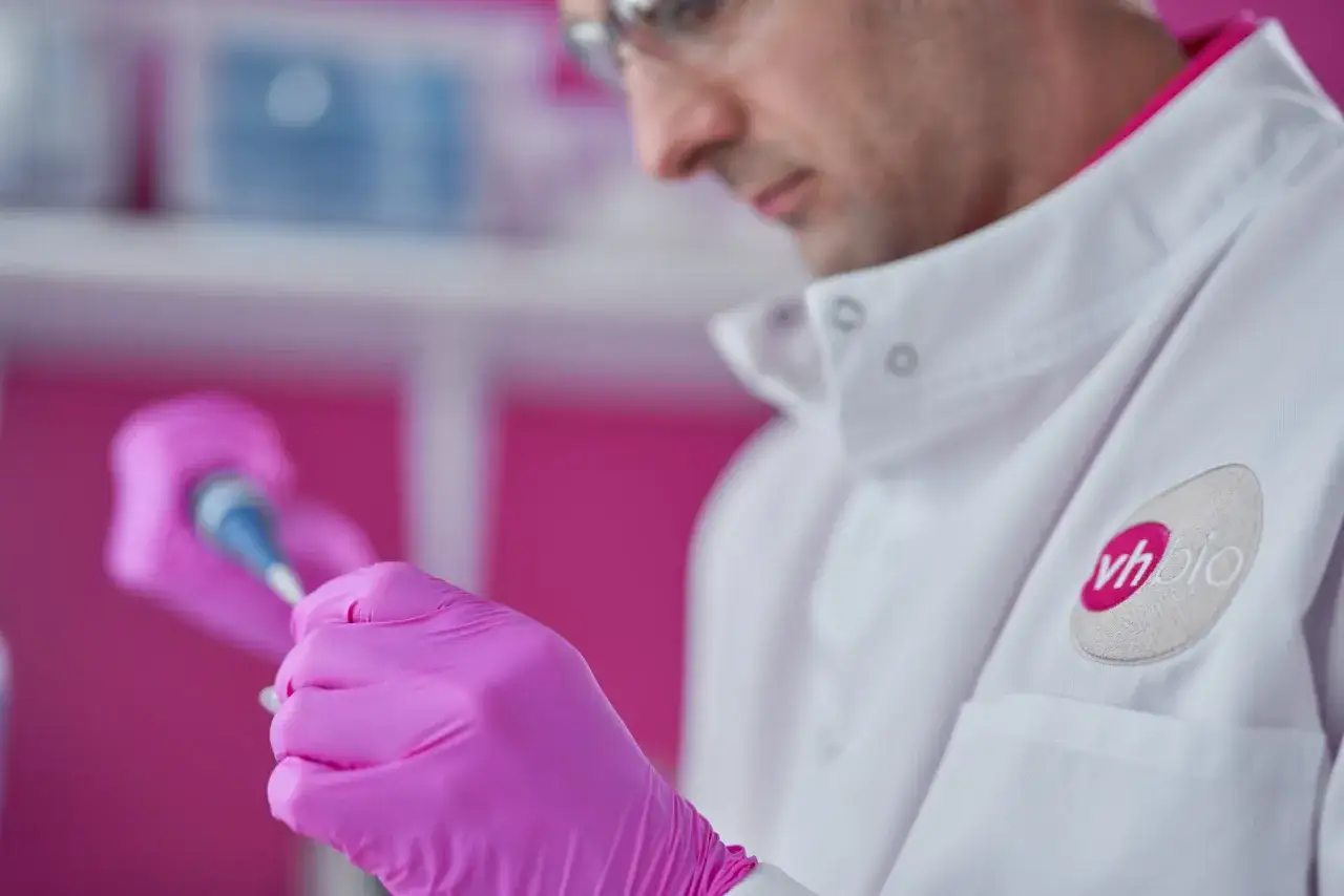 Científico con guantes rosas manipula pipeta, investigando el quimerismo genético en un laboratorio.