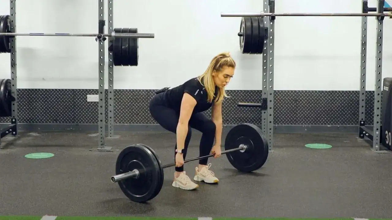 Donna si prepara per gli stacchi da terra con bilanciere in palestra.