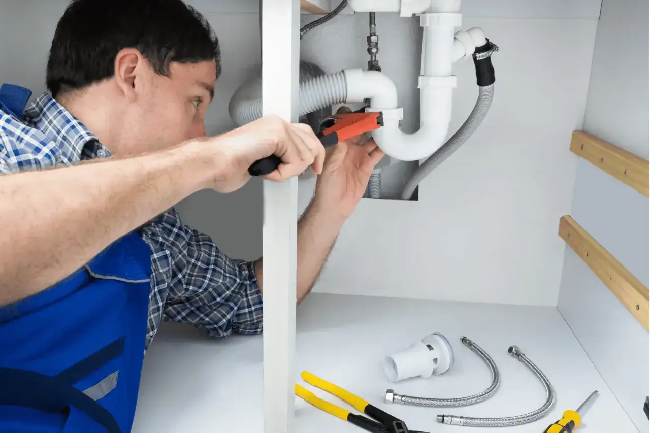Plumber working on pipes under a sink, a common step when learning how to increase water pressure.