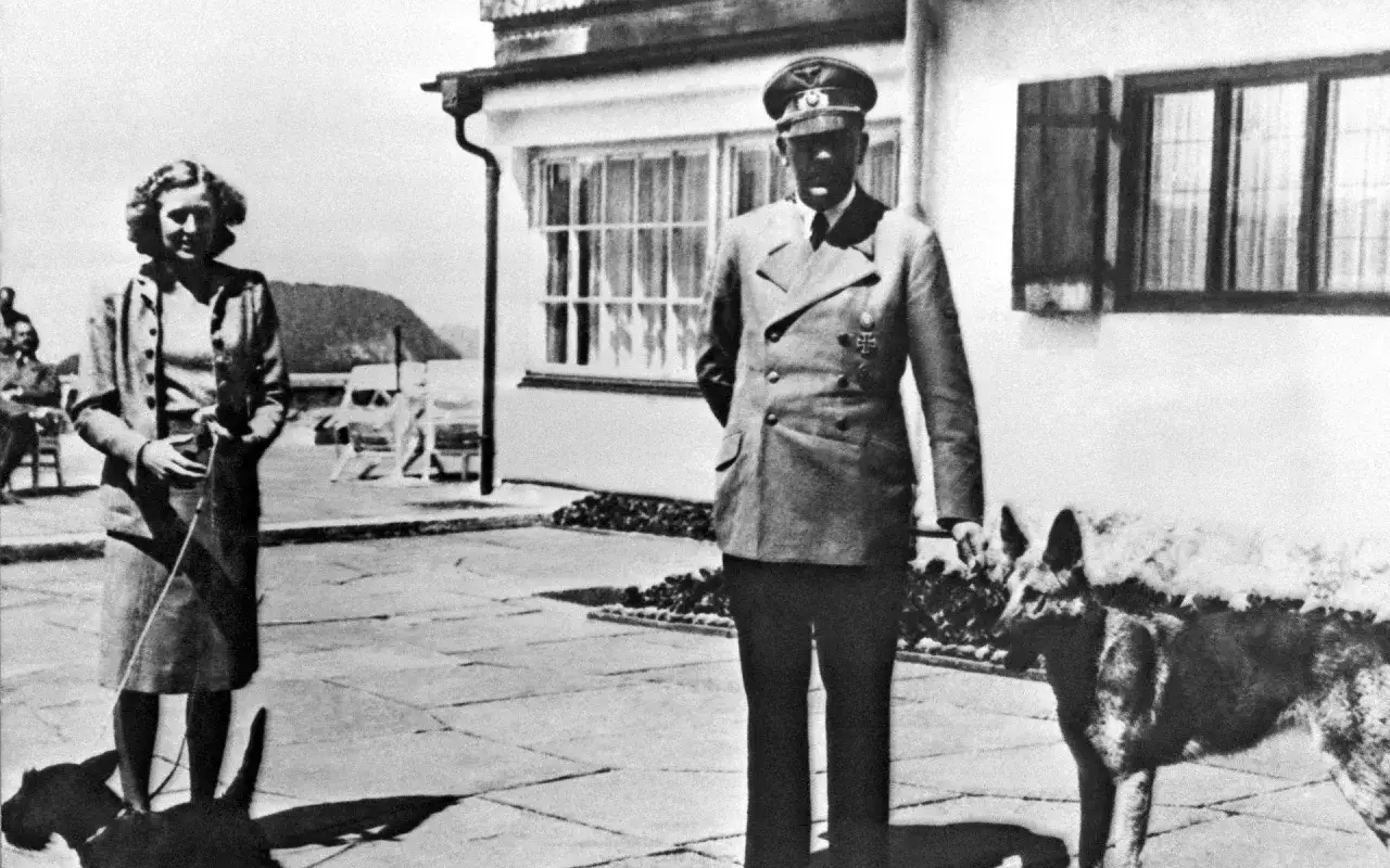 Eva Braun, hitlers fru, står med en hund framför ett hus.