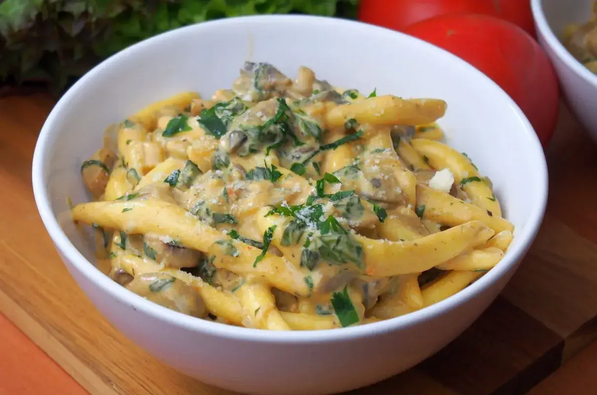 Pyszny makaron w sosie pieczarkowym, posypany natką pietruszki i parmezanem, podany w białej misce.