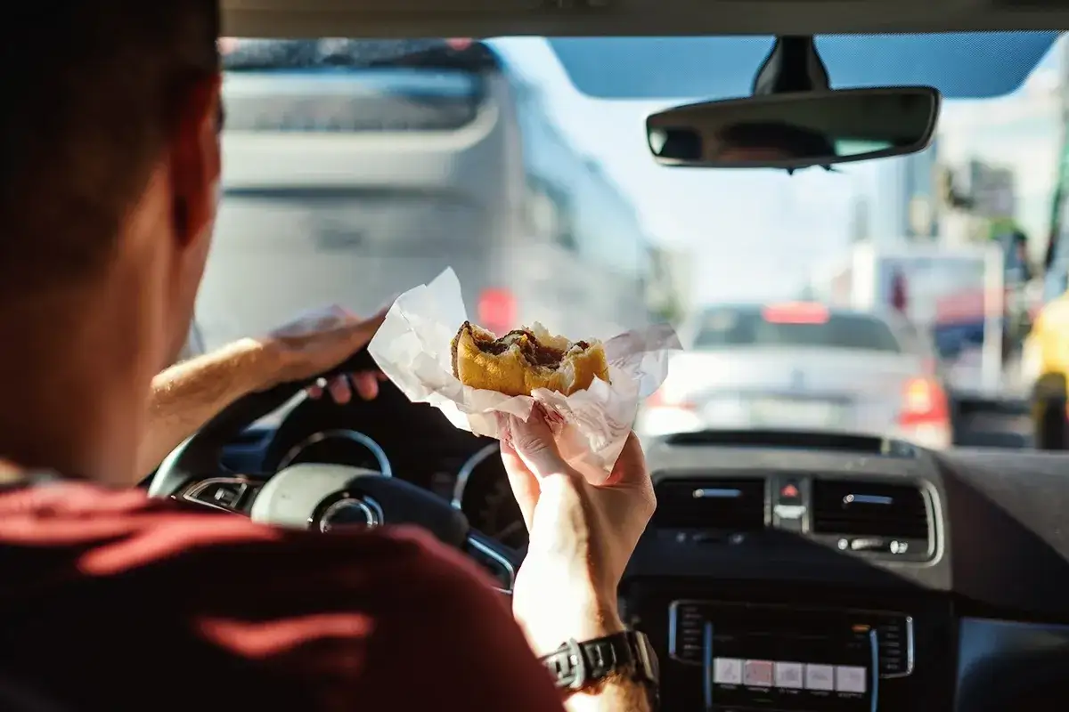 Uomo al volante mangia un panino in un ingorgo. Si può mangiare mentre si guida, ma attenzione alla sicurezza!