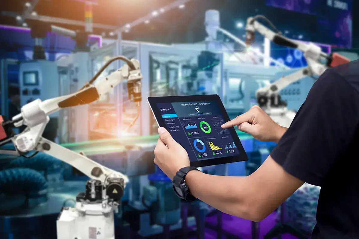 Ein Mann steuert Roboterarme mit einem Tablet. Das Display zeigt Daten zur 4. industriellen Revolution zusammenfassung.