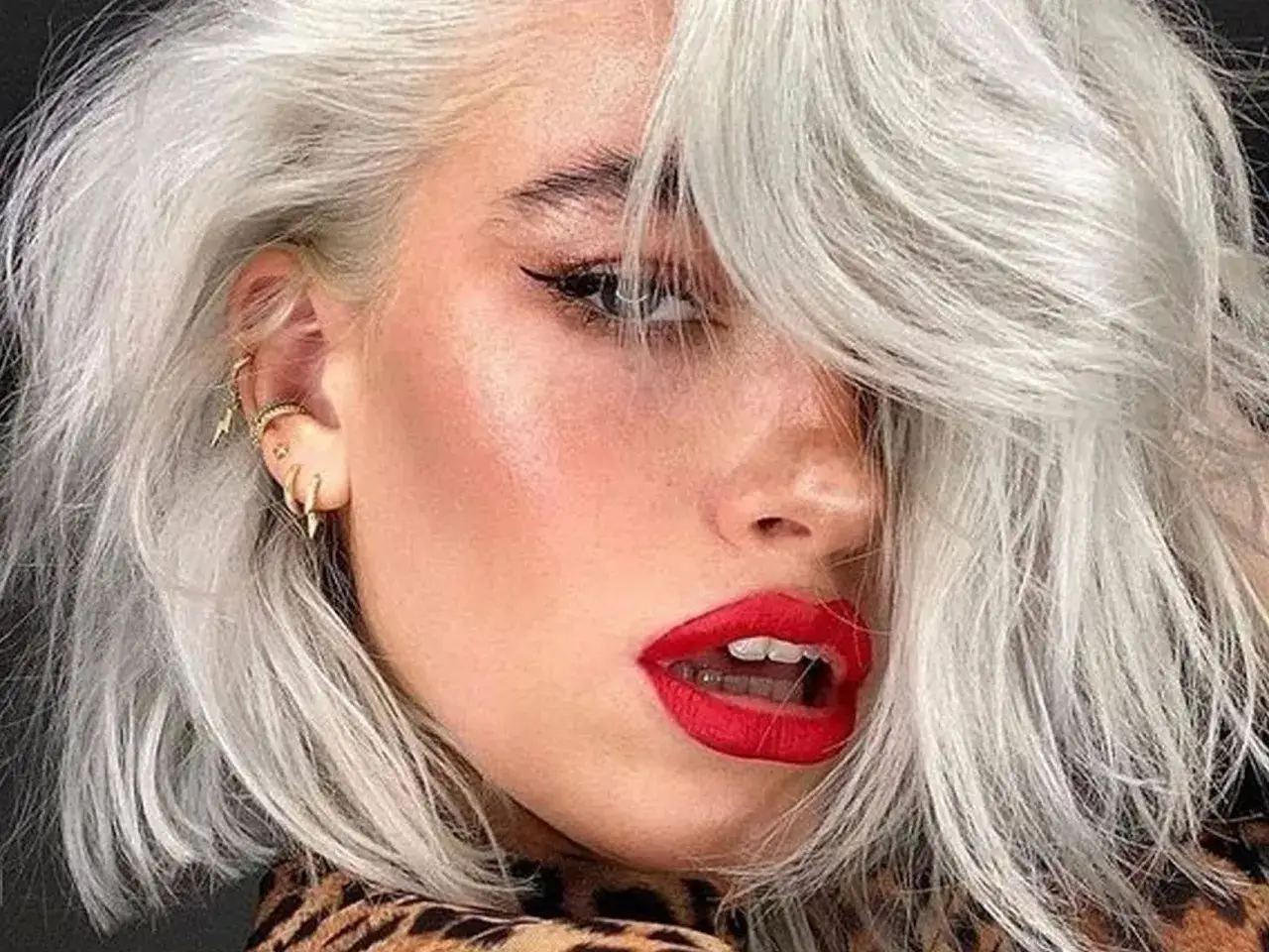 Mujer joven con pelo blanco plateado, labios rojos vibrantes y pendientes llamativos.