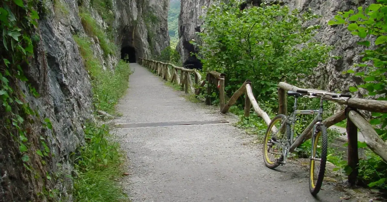 Bicicleta apoyada en la barandilla de madera en la senda del oso, un camino pedregoso que atraviesa un cañón rocoso con vegetación exuberante.