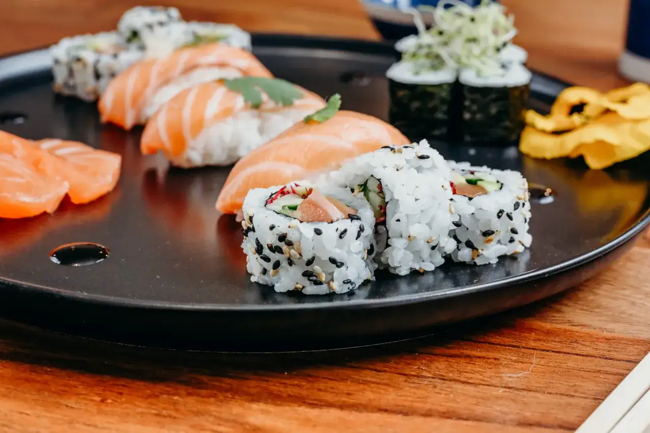 Różne rodzaje sushi: nigiri z łososiem, rolki z sezamem i warzywami, oraz maki z zielonymi kiełkami.