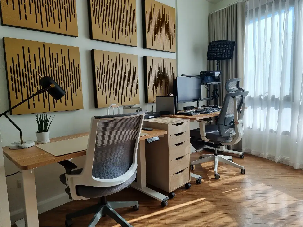 Nowoczesne biuro z dwoma stanowiskami pracy, ergonomicznymi krzesłami i dekoracjami na ścianie. Świetne pomysły na pokój dla pracujących zdalnie.
