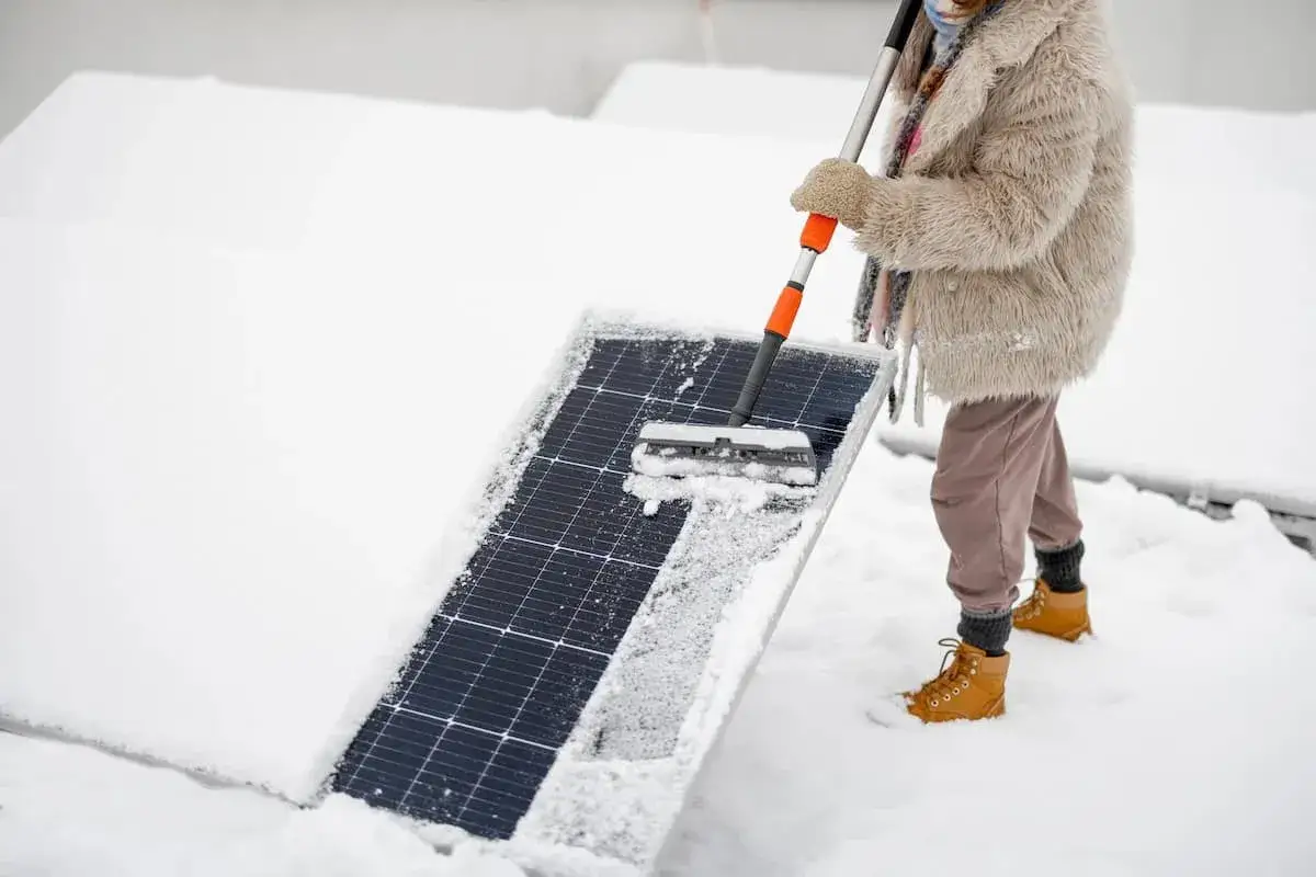 Person reinigt Solarmodul von Schnee, um im Winter heizen zu k&ouml;nnen.