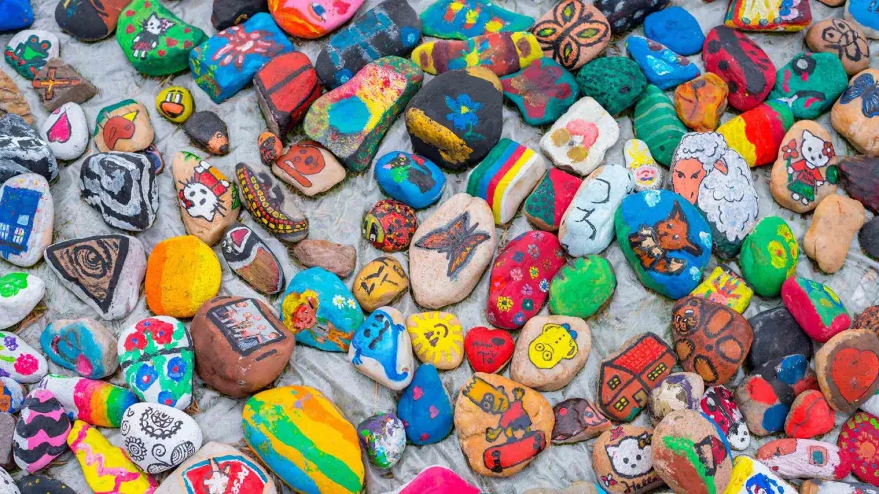 Bunte, bemalte Steine mit Motiven wie Hello Kitty, Häusern und Tieren. Eine Sammlung von Kunstwerken, die das **steine bemalen**-Hobby zeigen.
