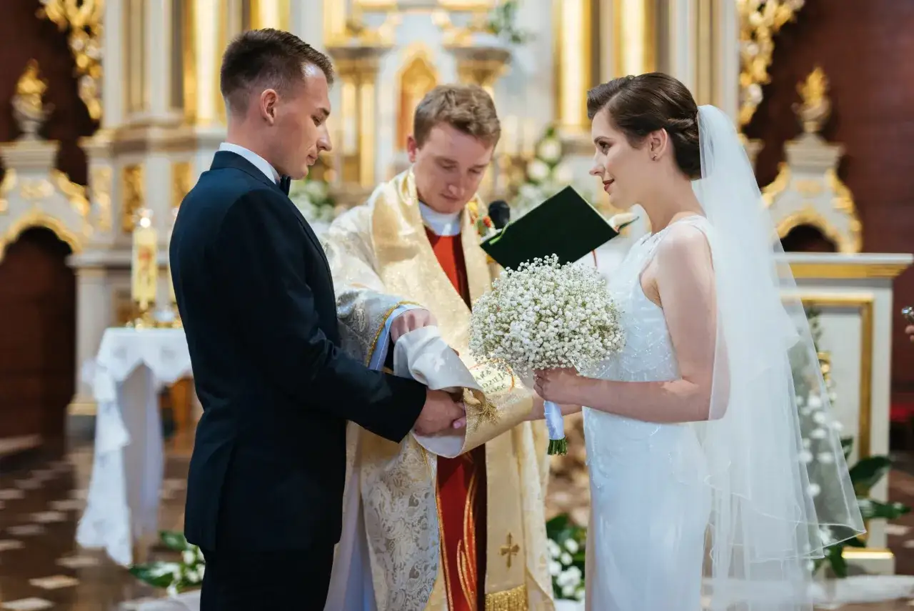 Panna młoda w białej sukni i welonie, z bukietem w dłoni, podczas ceremonii ślubnej.