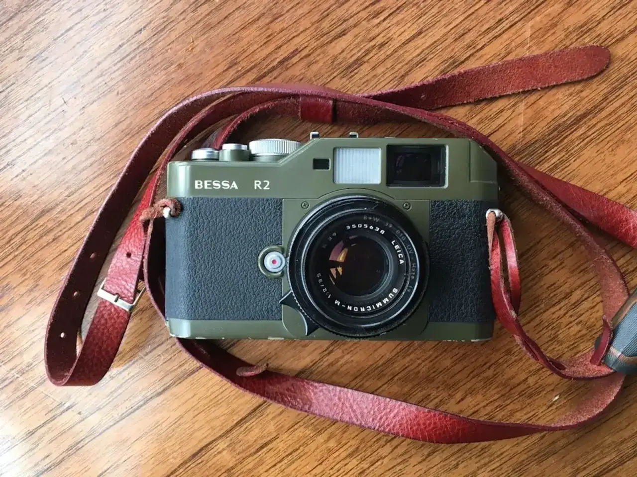 A vintage green Bessa R2 camera with a red leather strap rests on a wooden surface, ready for its next adventure.