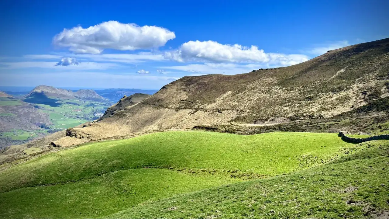 Verde prado en Ason Cantabria, con montañas ocres y cielo azul con nubes blancas.
