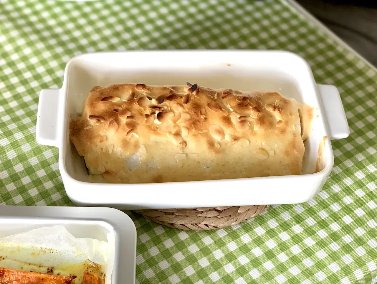 Bacalao gratinado con alioli, cubierto de almendras tostadas, listo para servir en su fuente blanca.