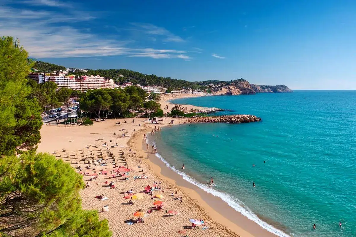 Piękna, słoneczna plaża na Costa Brava we wrześniu. Turkusowe morze, złoty piasek i zielone wzgórza tworzą idealną pogodę na wypoczynek.