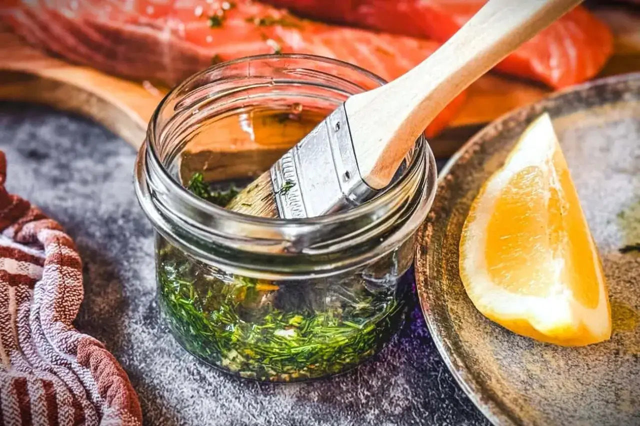Marinade mit Kräutern und Zitrone bereit, um Lachs zu verfeinern. Ein Pinsel liegt in der Glasflasche.