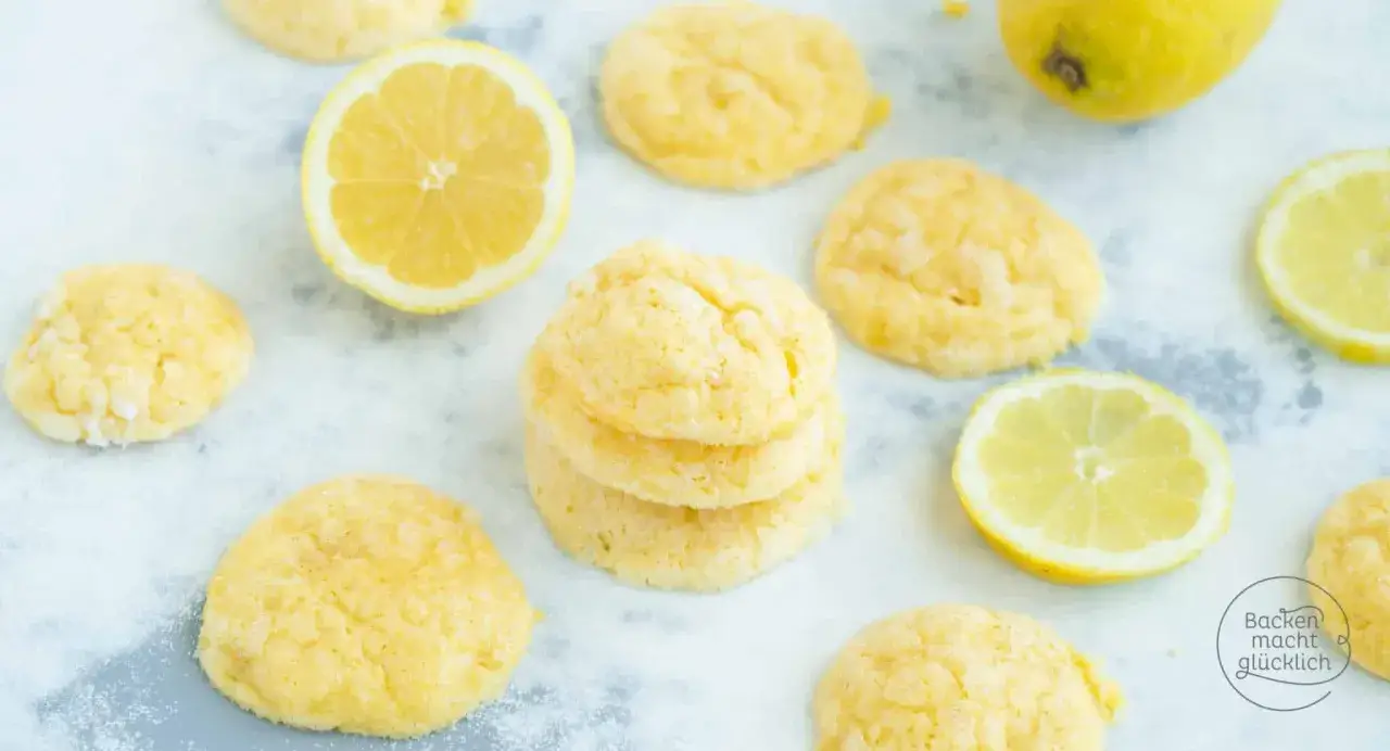 Zarte, zitronengelbe **lemon cookies** liegen verstreut neben frischen Zitronenscheiben auf einem hellen Untergrund.