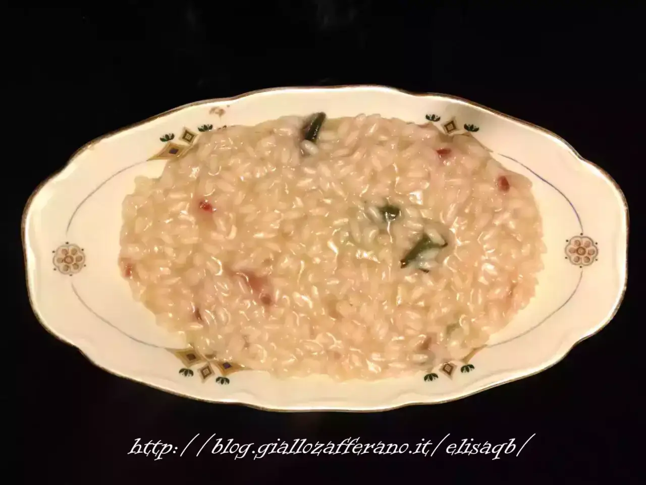 Un cremoso riso in cagnone, con pezzetti di pancetta e verdure, servito in un elegante piatto decorato.