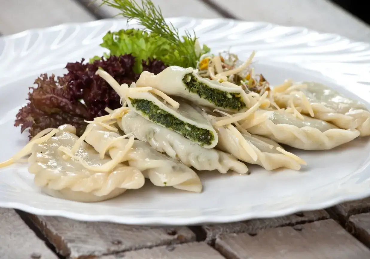 Pyszne pierogi ze szpinakiem i serem feta, udekorowane świeżymi ziołami i sałatką.