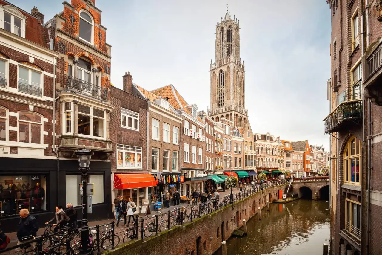 Utrecht altstadt mit Domtoren und Grachten. Menschen spazieren und radeln entlang der Wasserwege, umgeben von historischen Gebäuden.