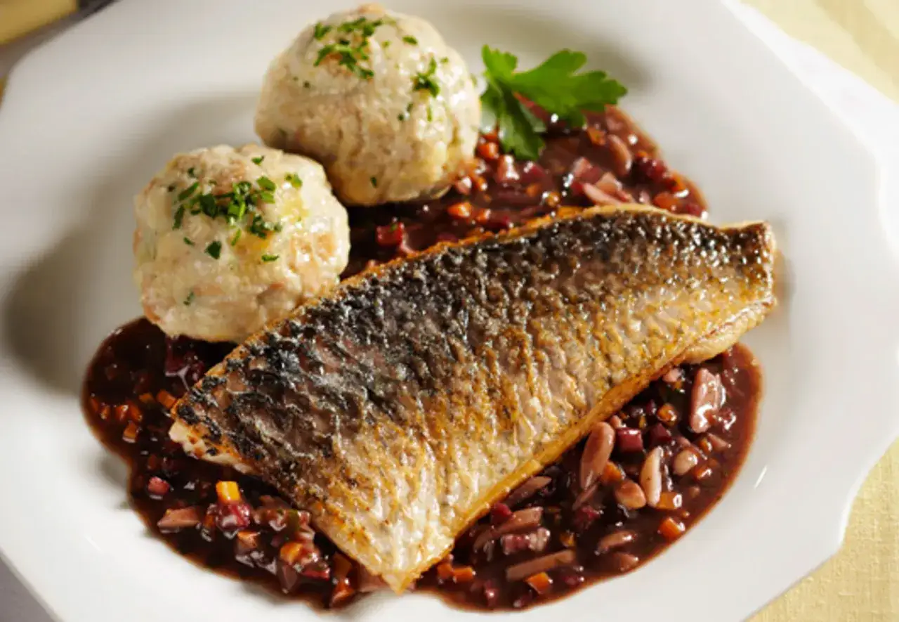 Gebratener Karpfen mit zwei Klößen und einer dunklen Soße mit Gemüse. Was isst man zu Karpfen? Klöße und Soße sind eine klassische Beilage.