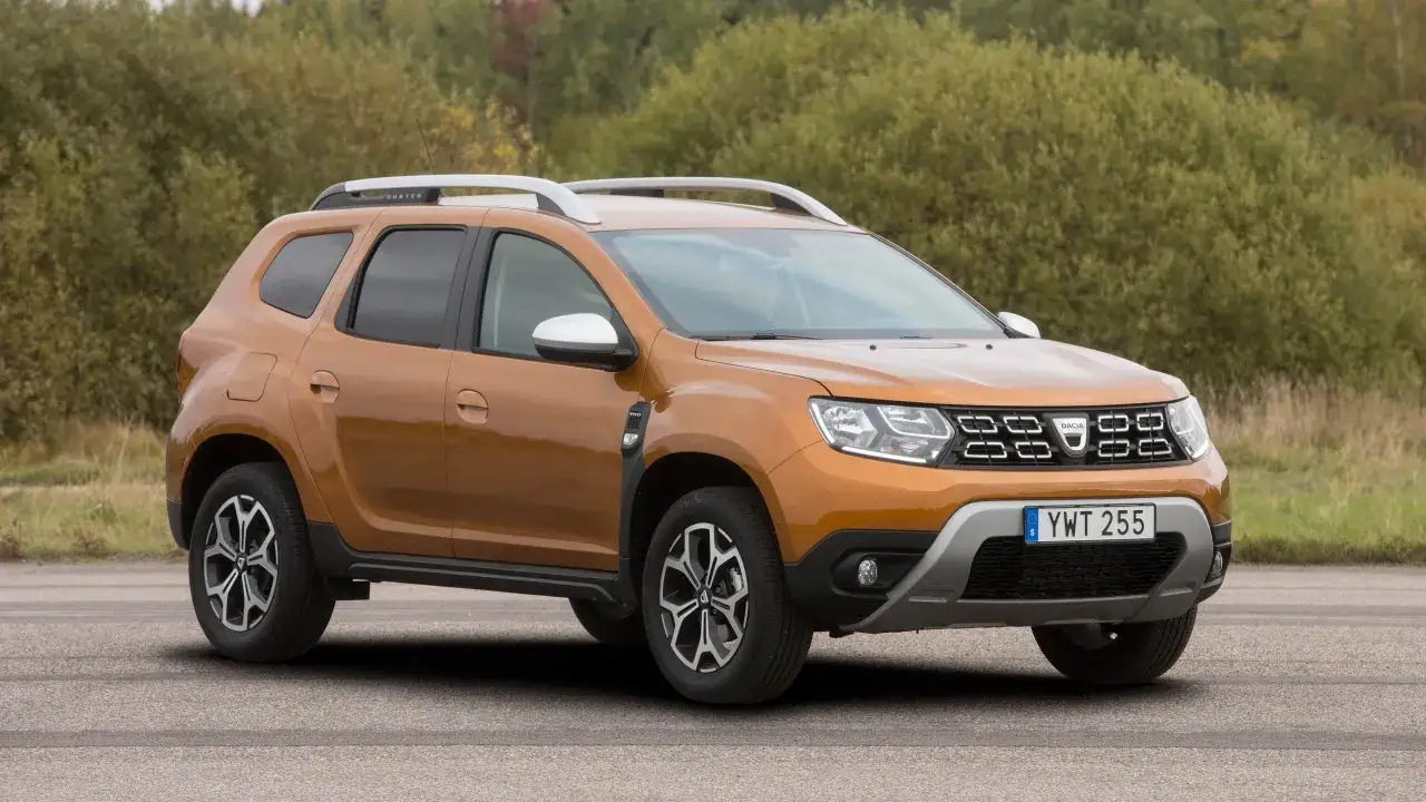 En orange Dacia Duster begagnad står parkerad utomhus. Bilen har takräcken och en 4WD-dekal.