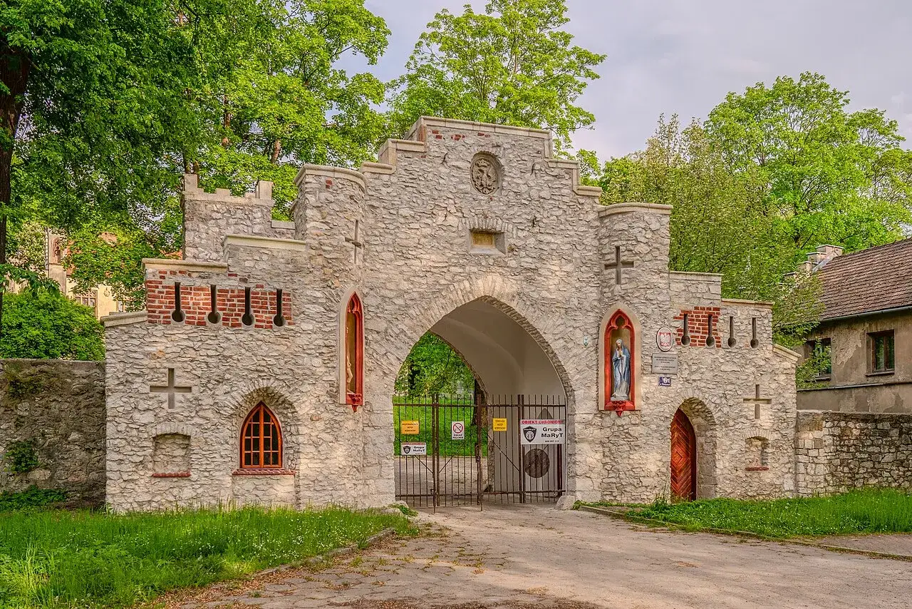 Kamienny pałac w Młoszowej, z bramą i wieżyczkami, otoczony zielenią.