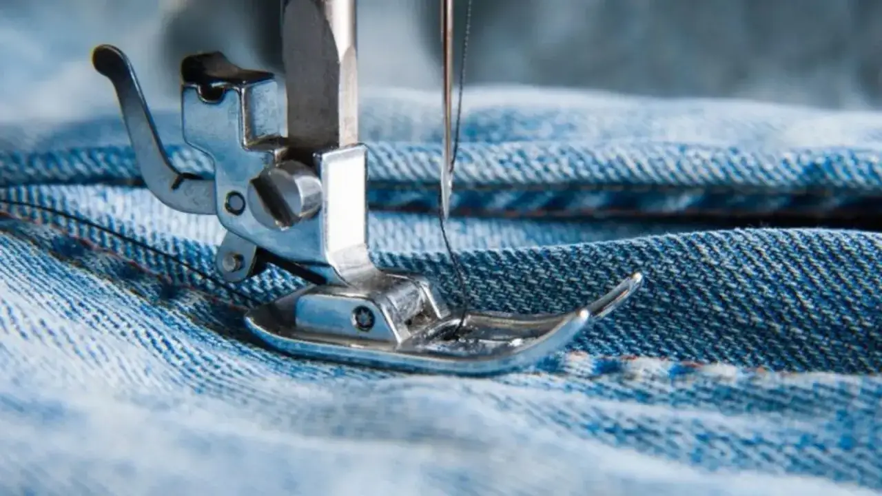 Gros plan sur une machine à coudre travaillant sur la fabrication du jean. La couture se fait sur le tissu denim bleu.